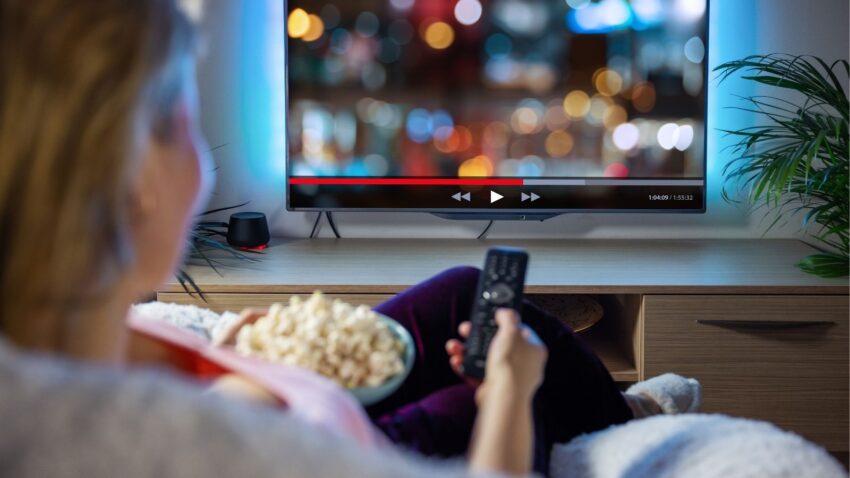 Kobieta ogląda telewizję w salonie z popcornem w ręku.
